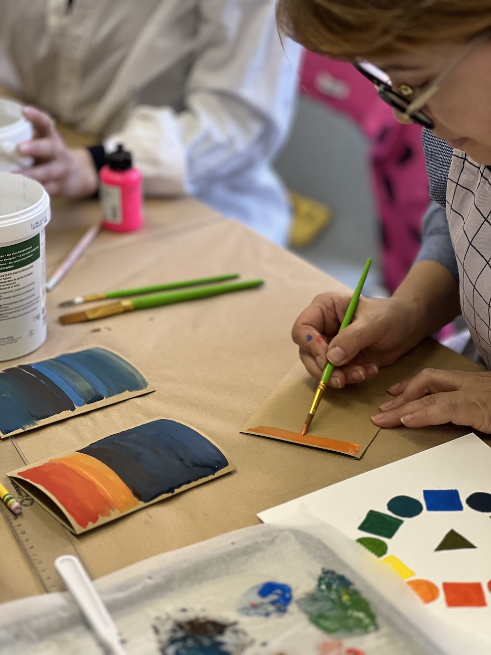 Man sieht eine Hand, die einen Pinsel hält und ein braunes Papier bemalt
